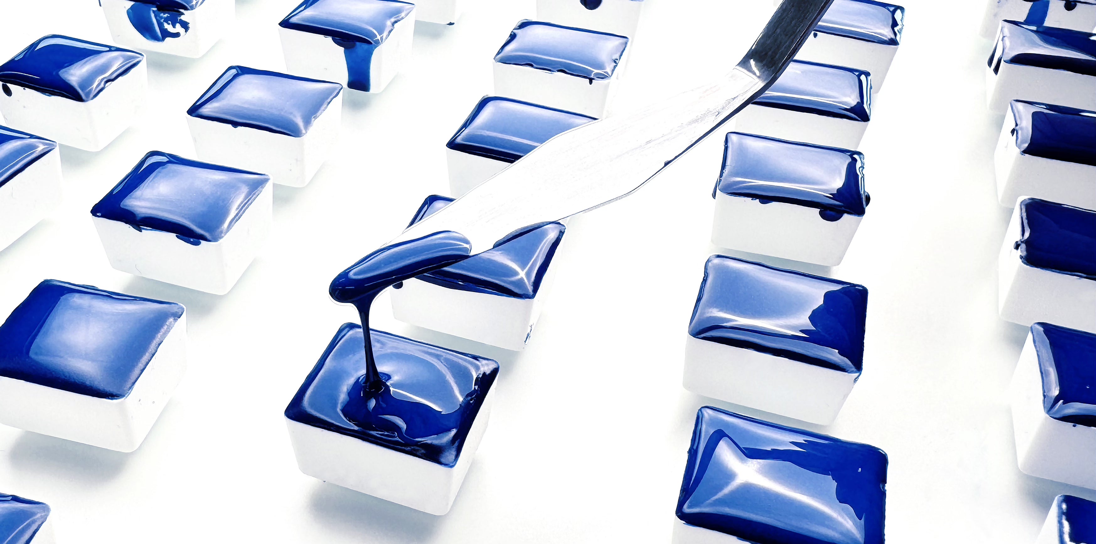 Hand pouring handmade blue watercolor paint into half pans over multiple layers