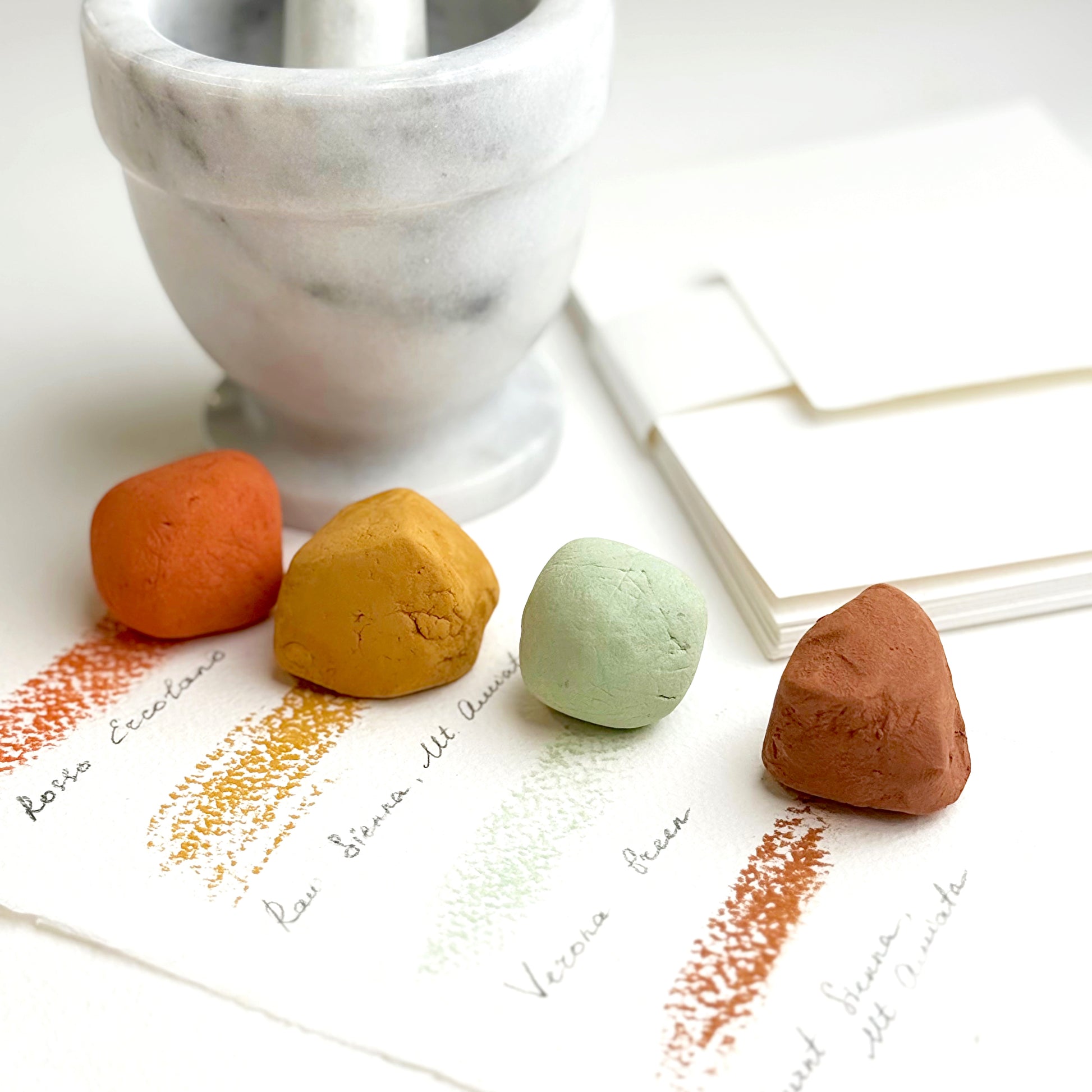 Four colorful pastel drawing stones on a marble surface with a white marble mortar and pestle.