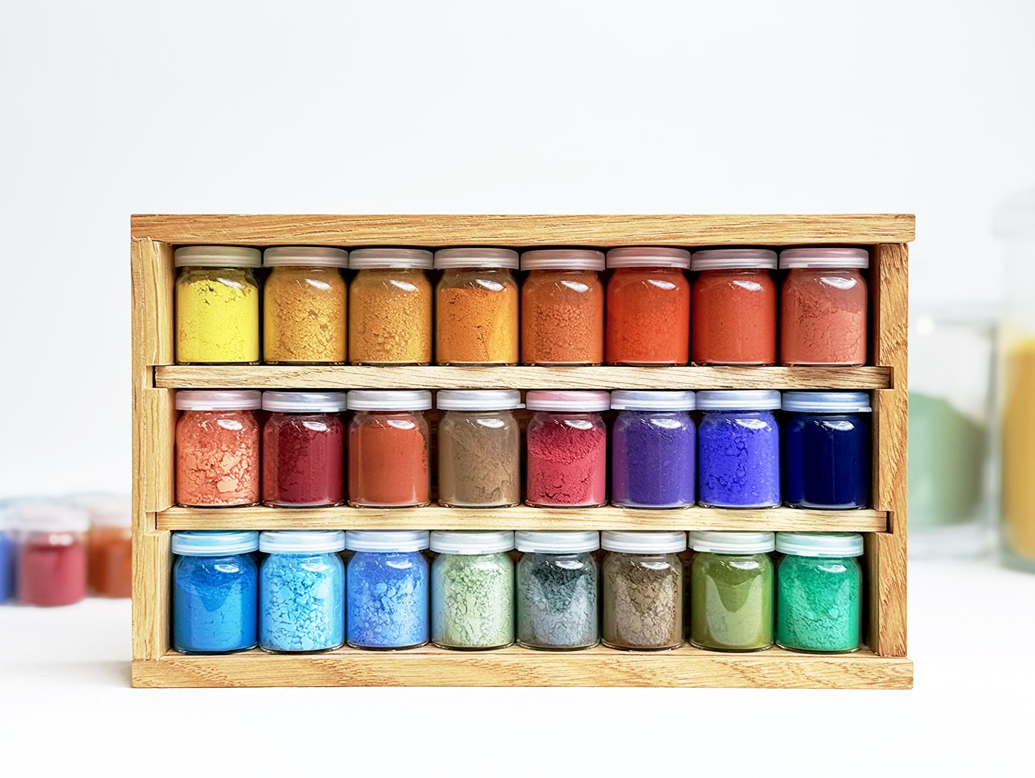 Set of 24 small jars with colorful contents in a wooden holder on a white background