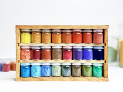 Set of 24 small jars with colorful contents in a wooden holder on a white background