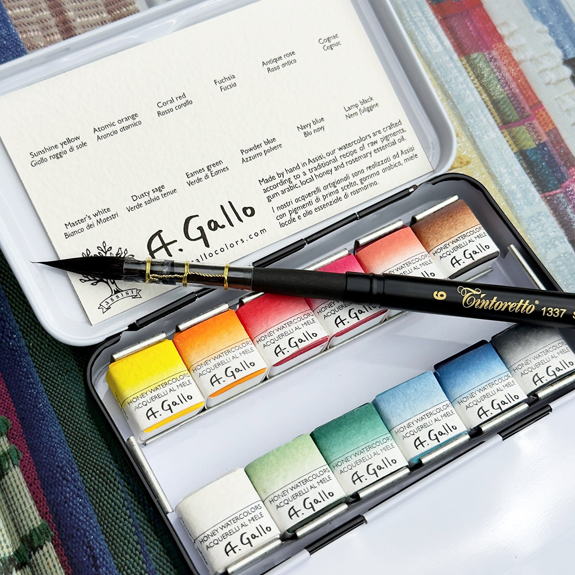A Gallo watercolor set with a brush on a textured fabric background