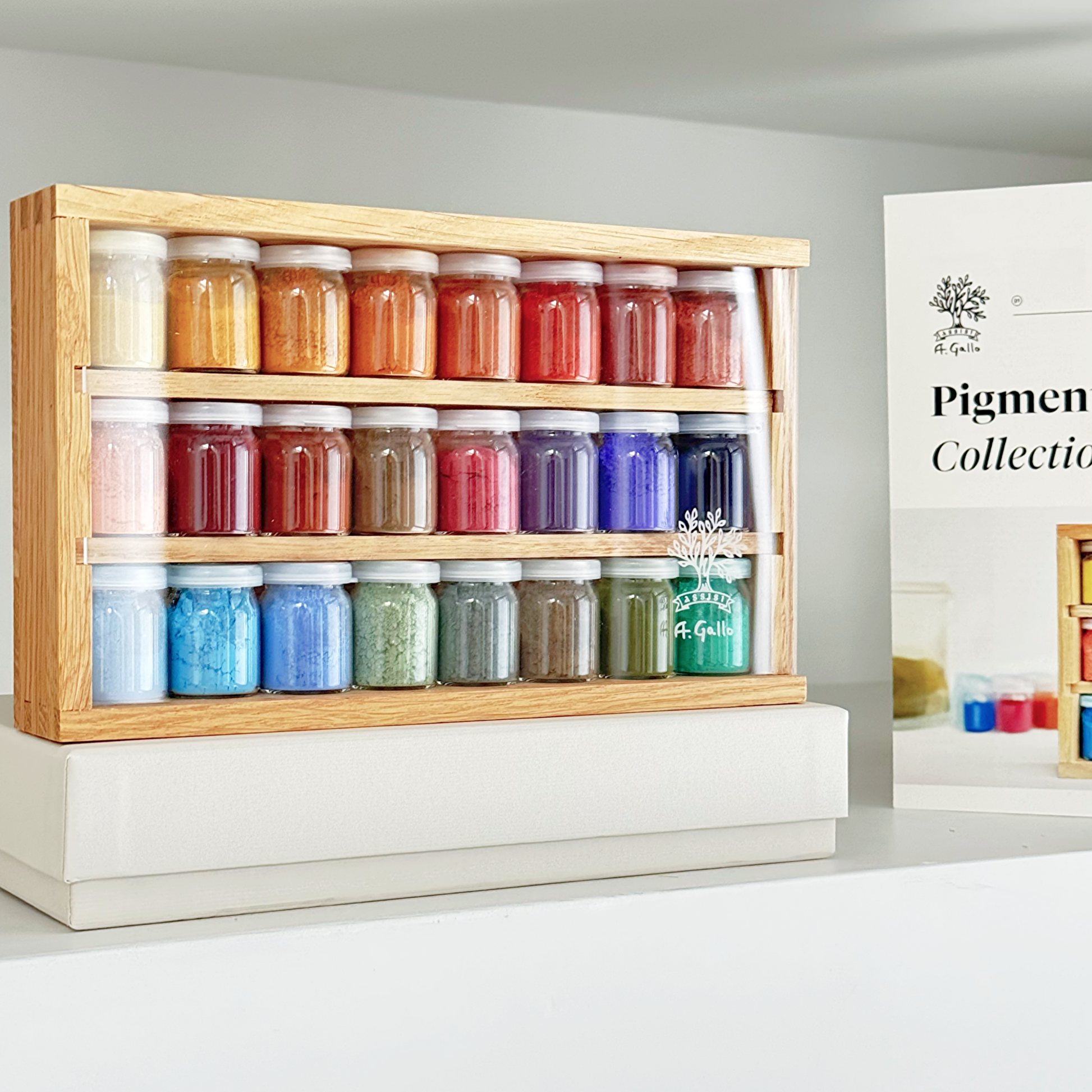 Wooden shelf with colorful jars of pigments and a 'Pigment Collection' sign in the background.