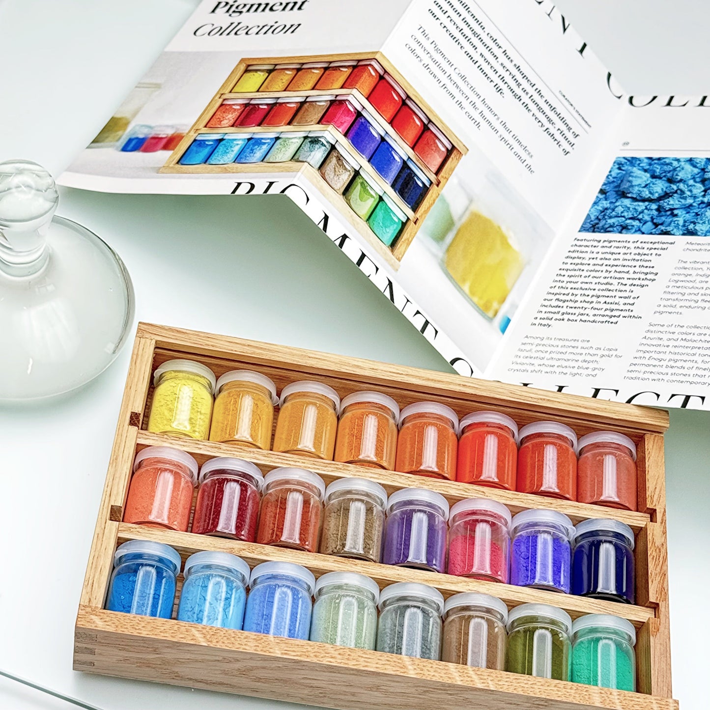 Set of colorful paint jars in a wooden box with an open magazine in the background.
