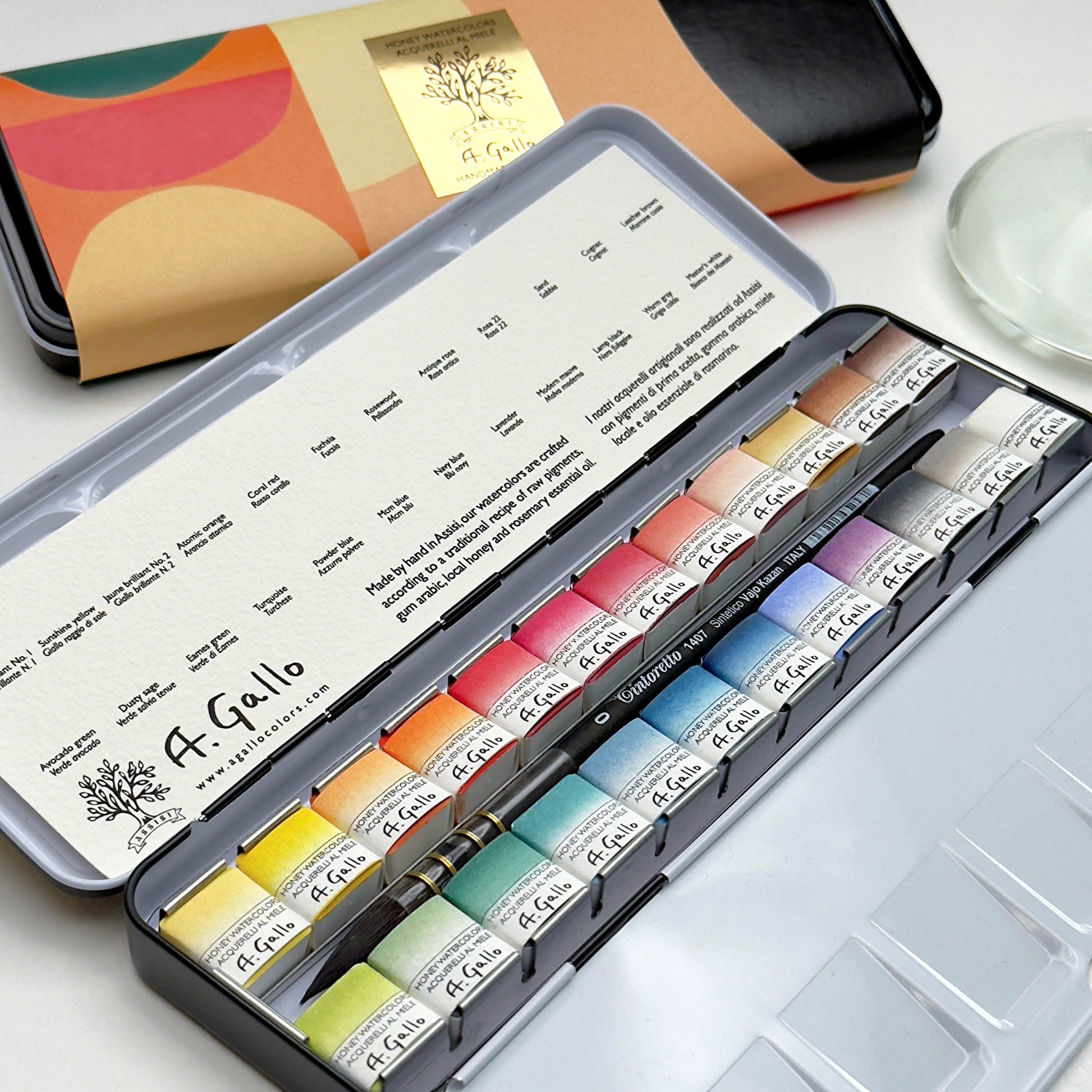Set of A. Gallo watercolor paints in a metal tin with a color swatch book in the background.