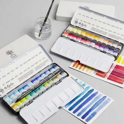An open set of watercolor paints in a white metal case, shown alongside closed cases, swatch cards, a paintbrush, and a small jar of water on a light gray background. The brand name 'L'Enseigne' is visible on the paint tubes.
